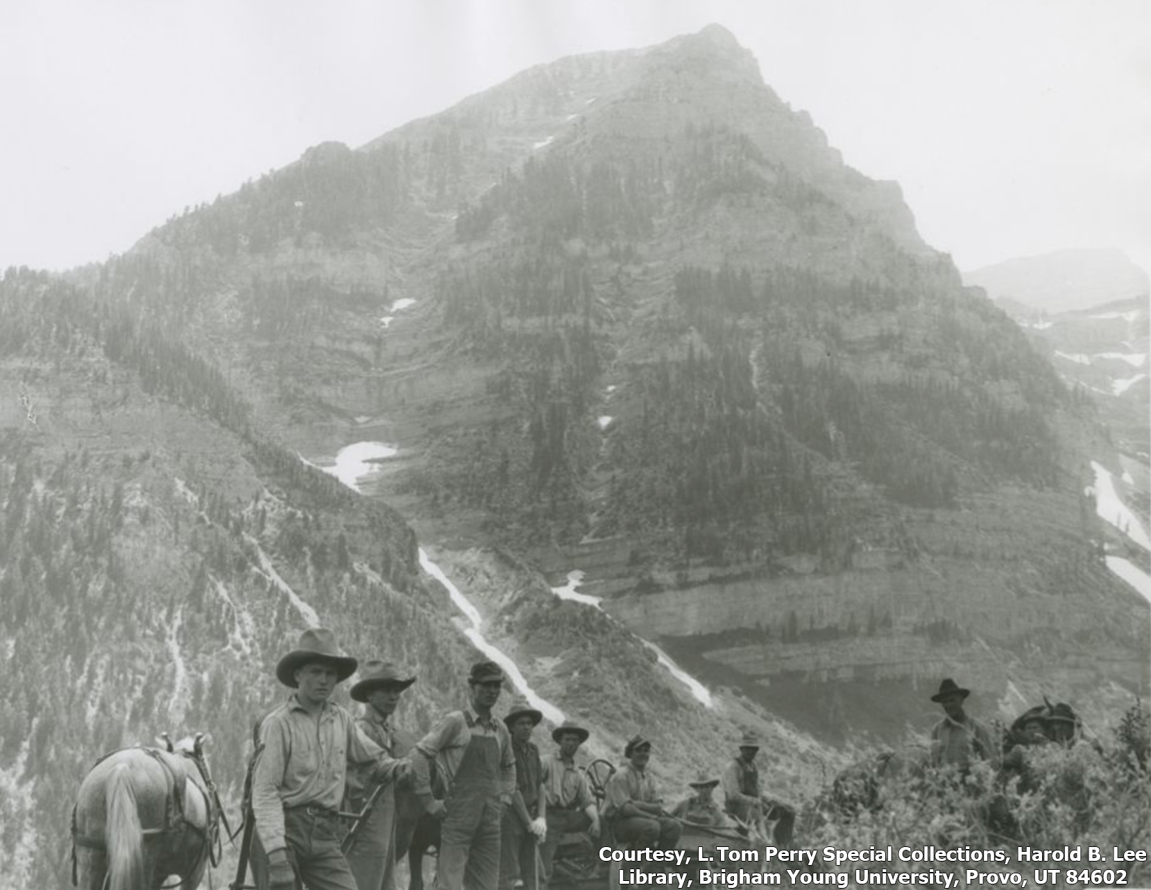 Men and horses stand with Roberts Horn in the background in this black and white photo